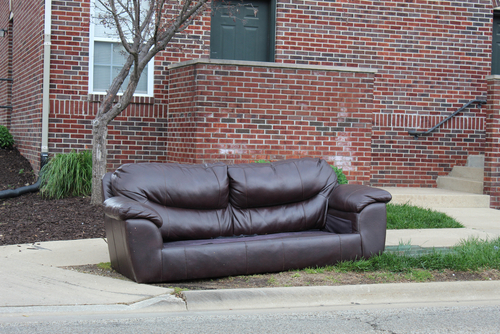 discarded,leather,couch,sits,on,curb,in,front,of,brick